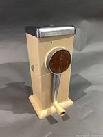 Front view of Ice-O-Mat ice crusher showing cream body, chrome lid, brown dial, ivory handle