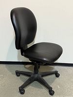 Front angled view of black low-back office chair showing seat, backrest and casters