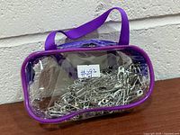 Clear vinyl pouch with purple trim filled with safety pins