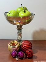 Pedestal bowl filled with faux apples, ornaments arranged in front