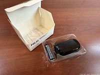 Open box with plastic tray holding black oximeter and two AAA batteries