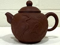 Full view of teapot front showing crane motif and lid with finial