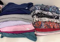 Stacked folded tops showing solid navy, grey, patterned paisley, abstract prints