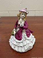 Front view of porcelain lady figurine showing magenta-pink gown, white ruffled skirt with red dots, pink hat, green purse