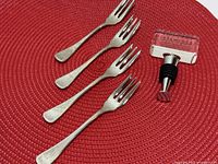 Overall view of four forks and wine stopper on red mat