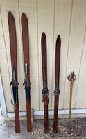 Two pairs of wooden skis and one wooden pole leaning against wall