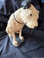 Front angled view of seated plaster Nipper dog showing collar, base and damage