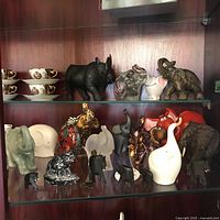 Full view of cabinet shelves showing assorted elephant figurines below tea cups