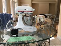 Overall view of mixer, bowl, attachments, recipe book and measuring cups on glass table