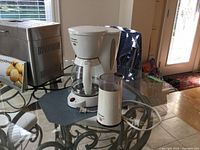 Coffee maker and grinder beside bread maker on glass table