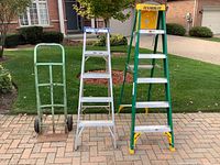 Front view of all three items: green dollie, silver 5-ft ladder, green/yellow 6-ft ladder