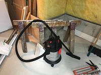 Overall view of two wooden sawhorses and Benchmark shop vacuum with hose and accessories