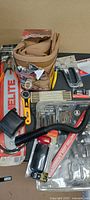Group shot showing chainsaw bar, strap, staple gun, bit sets, rotary cutter, hose, timer