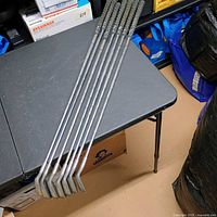 Full view of seven Ping irons laid side by side on table