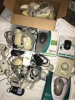 Overview of boxed and loose mice including cardboard box filled with assorted wired mice and additional packaged items