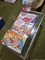 All four sealed games on table: Operation, Candy Land, Guess Who?, UNO deck