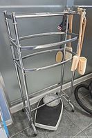 Front view of chrome towel rack with loofah scrubbers hanging and scale underneath