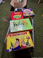 Four board games stacked on a cart: Apples to Apples, Cranium, Partini, Battle of the Sexes