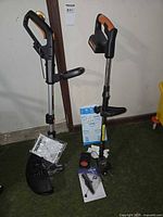 Two cordless trimmers standing with accessories on floor