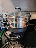 Full set stacked on stove showing base pan, two steamer baskets, glass lid