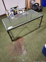 Full view of coffee table showing glass top, metal frame, ringed legs, and X stretcher