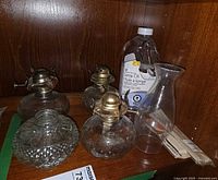Overview of four glass lamp fonts, three brass burners, chimney, oil bottle, wick packs