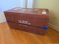 Overall view of painted wooden trunk with latch, stencil and blue corner guards