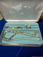 Open jewelry case showing gold-tone and silver-tone pieces in blue lining