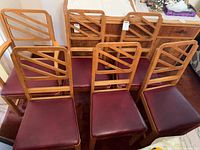 front view of six wooden chairs showing geometric backs and burgundy seats