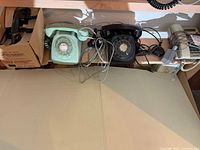 Mint green rotary phone, black rotary phone, beige phone, boxed handset plus cords on shelf