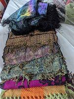 Stack of assorted scarves and shawls, top view showing varied colors and fringe