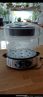 Assembled steamer showing base, two stacked clear trays, vented lid, power cord visible