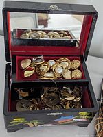 open lacquered jewelry box filled with gold-tone costume pieces