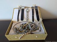 Open jewelry box displaying watches clipped to lid and tangle of jewelry inside