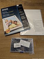 Epson glossy photo paper box, Canon matte photo paper pack behind, plastic organizer with black safety pins