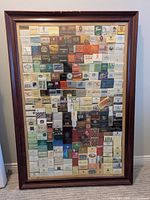 Full view of framed matchbook collage showing wood frame and glass front with grid of matchbooks