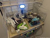 Overview of lot showing bulbs, cords, tools, umbrellas, tape, masks, batteries on small stand