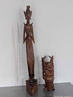 Front view tall Balinese goddess and smaller wood Buddha with ruler for scale