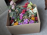 Large cardboard box filled with mixed artificial flowers in various colors