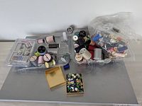 Overall lot view with trays of thread spools, bag of spools, gold box of sequins
