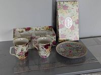 Two floral mugs, millefleur plate, floral gift box shown together with ruler for scale