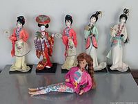 Front view of five Asian fabric dolls on stands and one Barbie doll