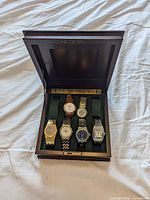 Box open showing six wristwatches seated in green felt slots