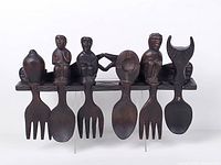 Front view of entire carved wooden wall hanging with six utensil shapes and carved figures