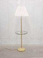 Full view of brass floor lamp with glass table and shade