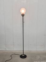 Full view of lamp lit showing glass bulb shade, pole, and base