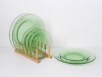 All seven green glass plates on wooden rack and one stacked set