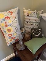 Two embroidered lumbar pillows and small decorative oil lamp on wooden table