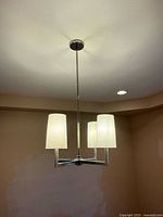 Full view of chrome chandelier hanging from ceiling showing three of the four cylindrical shades and central downrod