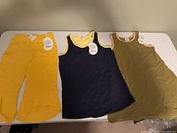 Overview of yellow pants, navy dress, olive dress laid flat on table